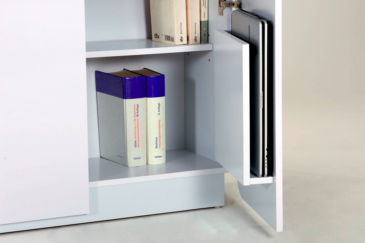Nahaufnahme eines weißen Schranks mit geöffneter Tür, die Bücher und einen Laptop zeigt. Perspektive von vorne rechts.