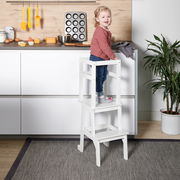 Ein weißer Lernturm in einer Küche, auf dem ein kleines Kind steht. Der Lernturm ist von der Seite zu sehen.