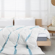 Een wit, volumineus gewatteerd dekbed met lichtblauwe accentstrepen op een houten bed in een lichte slaapkamer, gefotografeerd vanuit een vooraanzicht, licht van bovenaf.