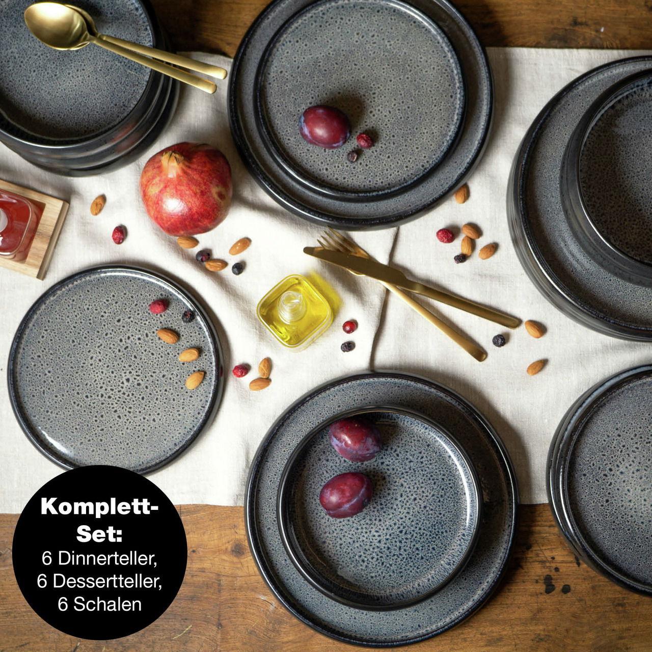 Vogelperspektive auf ein 18-teiliges graues Tafelservice-Set mit Tellern und Schalen, dekoriert mit Früchten und Nüssen auf einem Holztisch.