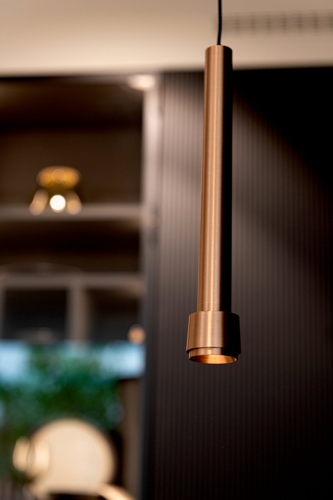 Lucide LED-Hängeleuchte für Stromschiene LINIAL Schlanke, zylindrische Pendelleuchte in Kupfer/Metalloptik mit warmem Licht, Nahaufnahme aus leicht seitlicher Perspektive vor unscharfem Innenraumhintergrund