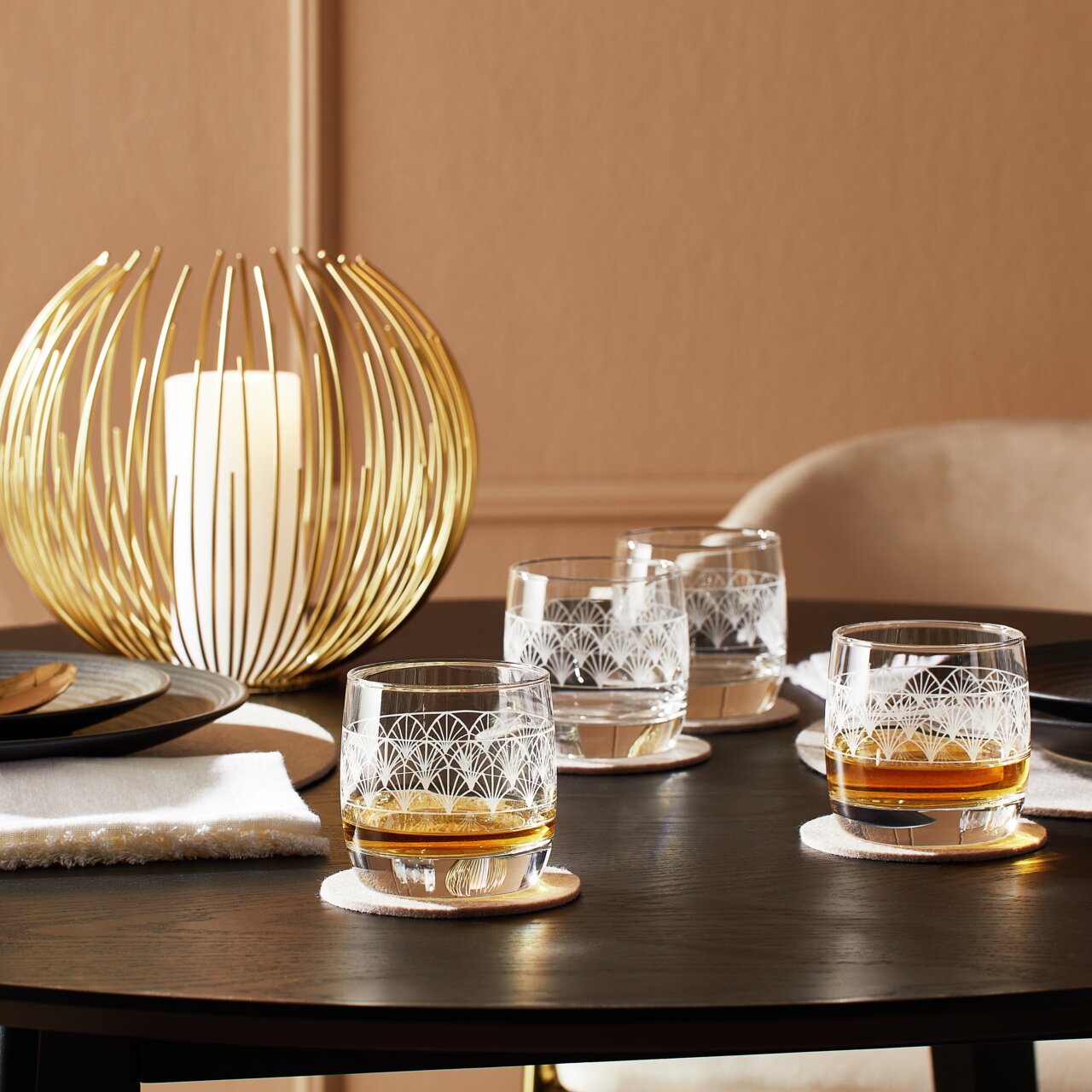 Vier Whiskybecher aus dem Paradisio 4er-Set auf einem gedeckten Tisch, mit einem goldenen Kerzenhalter im Hintergrund, aus seitlicher Perspektive fotografiert.