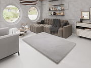 Moderner Wohnraum mit grauem Fellteppich in der Mitte, umgeben von einem beigen Sofa und stilvollen Dekorationen. Perspektive von schräg oben.