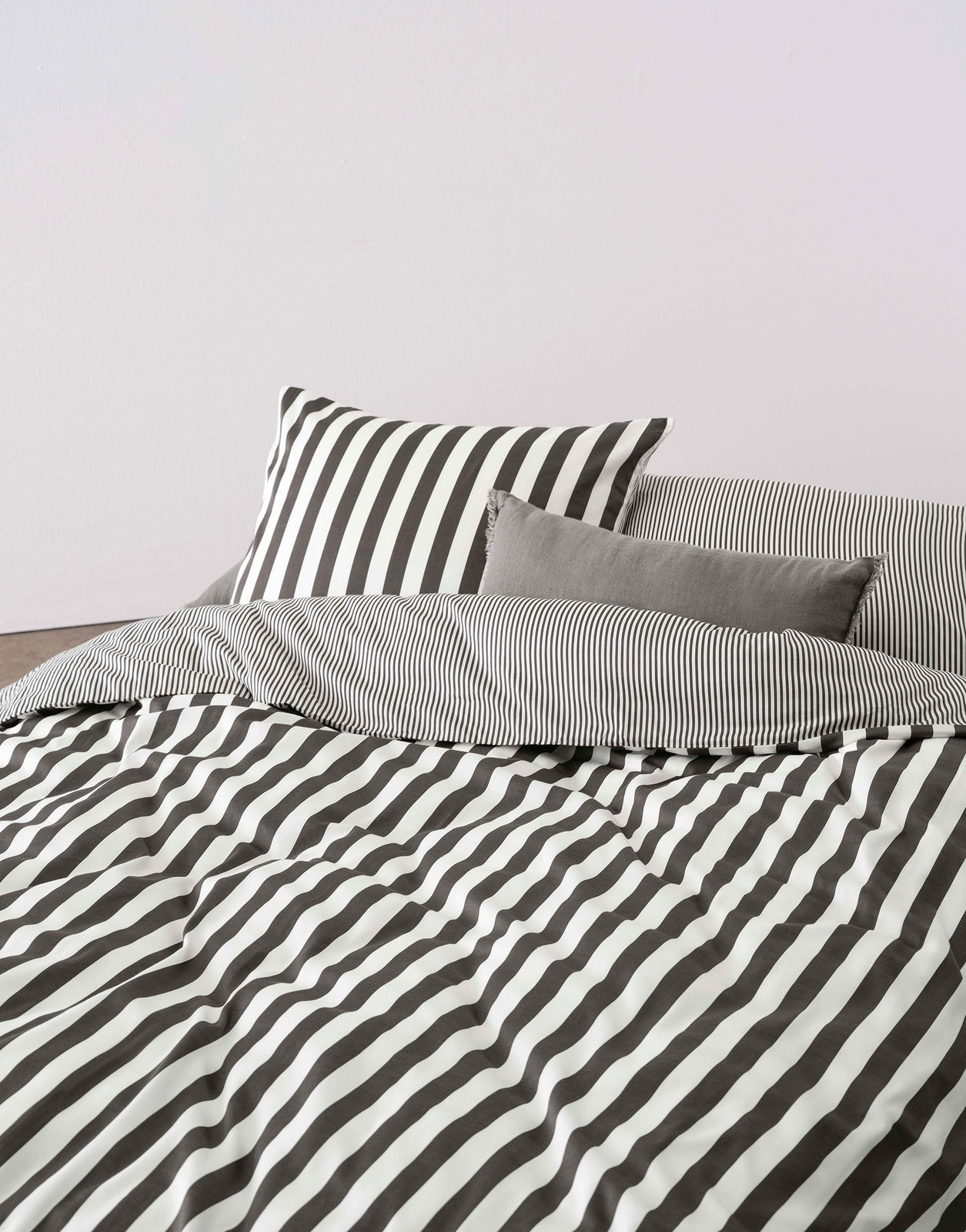 Bettwäsche-Set mit schwarz-weißen Streifen, bestehend aus einem Kissenbezug und einer Decke, aus der Perspektive von vorne fotografiert.