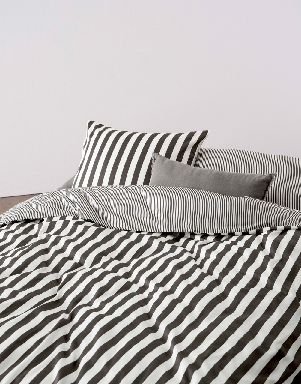 Bettwäsche-Set mit schwarz-weißen Streifen, bestehend aus einem Kissenbezug und einer Decke, aus der Perspektive von vorne fotografiert.