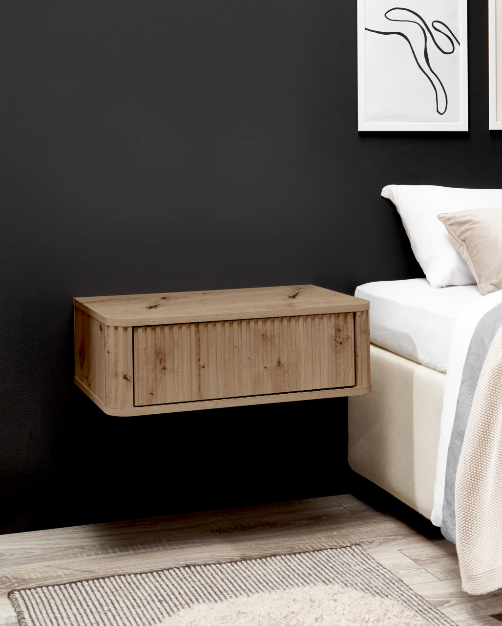 Z2 Nachtkommode GARI Schwebender Nachttisch aus hellem Holz mit Klappe/Schublade an dunkler Wand neben einem Bett, seitliche Perspektive.