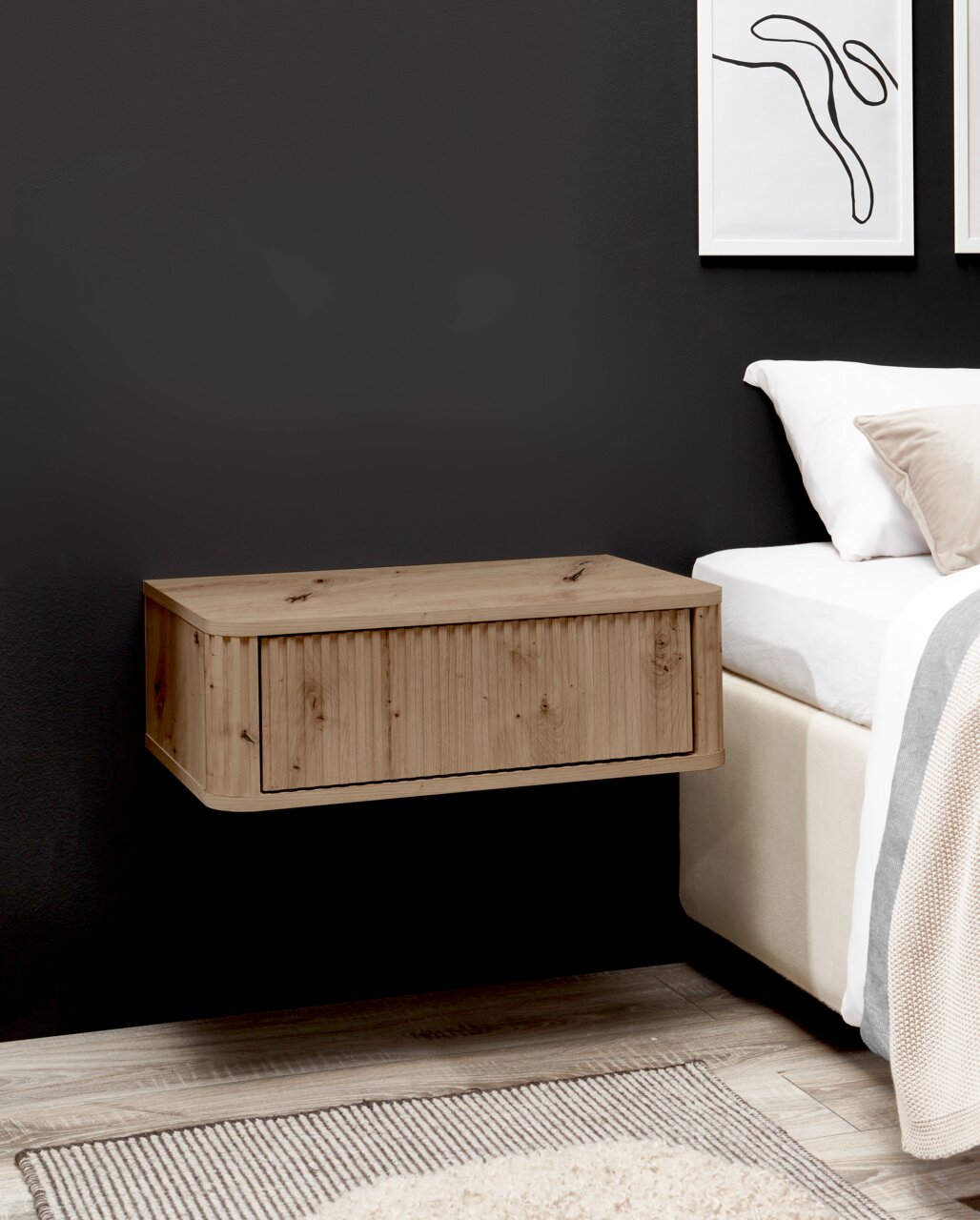Z2 Nachtkommode GARI Schwebender Nachttisch aus hellem Holz mit Klappe/Schublade an dunkler Wand neben einem Bett, seitliche Perspektive.