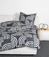 Bettwäsche-Set Janine PALERMO in Schwarz-Weiß mit geometrischem Muster, auf einem weißen Sofa drapiert, seitliche Perspektive