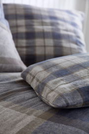 Nahaufnahme von karierten Bettwäsche in Blau- und Grautönen, perspektivisch von der Seite aufgenommen.