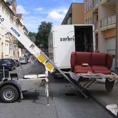 Ein Umzugswagen mit einem Außenlift, der eine rote Couch auf einer Straße in der Stadt auflädt.