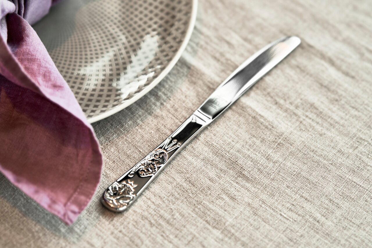 Kinderbesteck Messer mit Märchenmotiven, auf einem Tisch mit Teller und Serviette, von oben betrachtet.