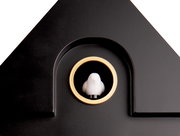 Nahaufnahme einer schwarzen Wanduhr mit einem goldenen Ring und einer kleinen weißen Figur in der Mitte, die wie ein Vogel aussieht. Die Perspektive zeigt die obere Hälfte der Uhr.