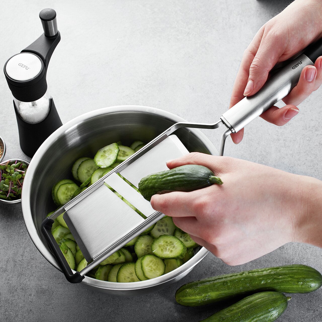 Gemüse- und Kartoffelhobel in der Hand, der Gurken in einer Schüssel aus Edelstahl schneidet, seitliche Perspektive.