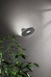 Moderne LED-Außenwandleuchte an einer Wand, seitliche Perspektive, mit Pflanzen im Vordergrund.