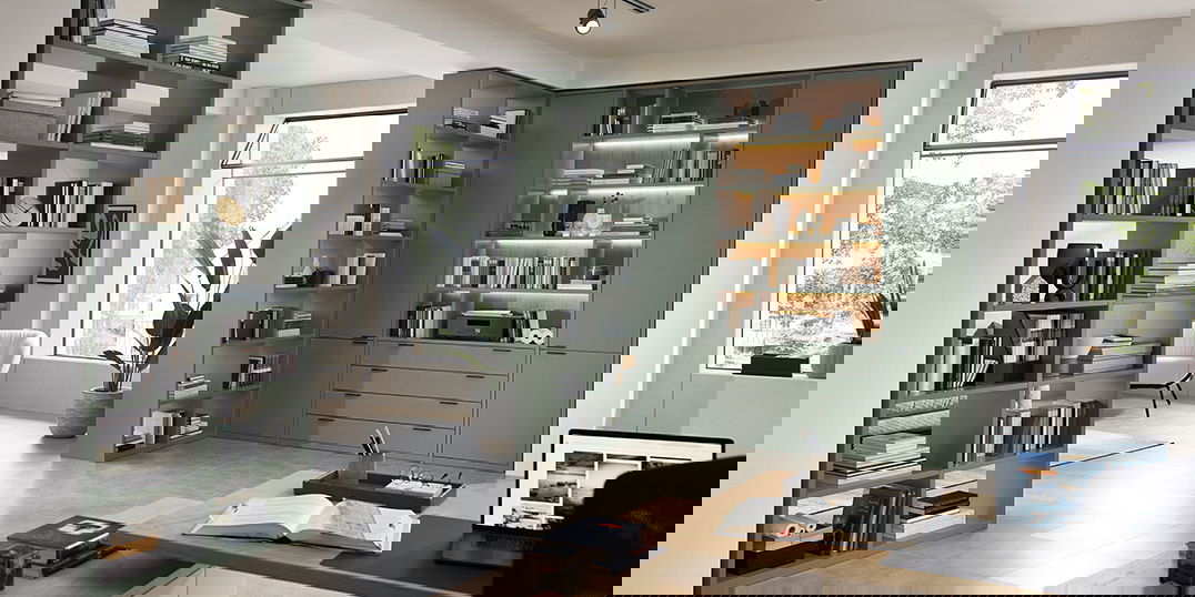 Modernes Heimbüro mit grünen Bücherregalen.