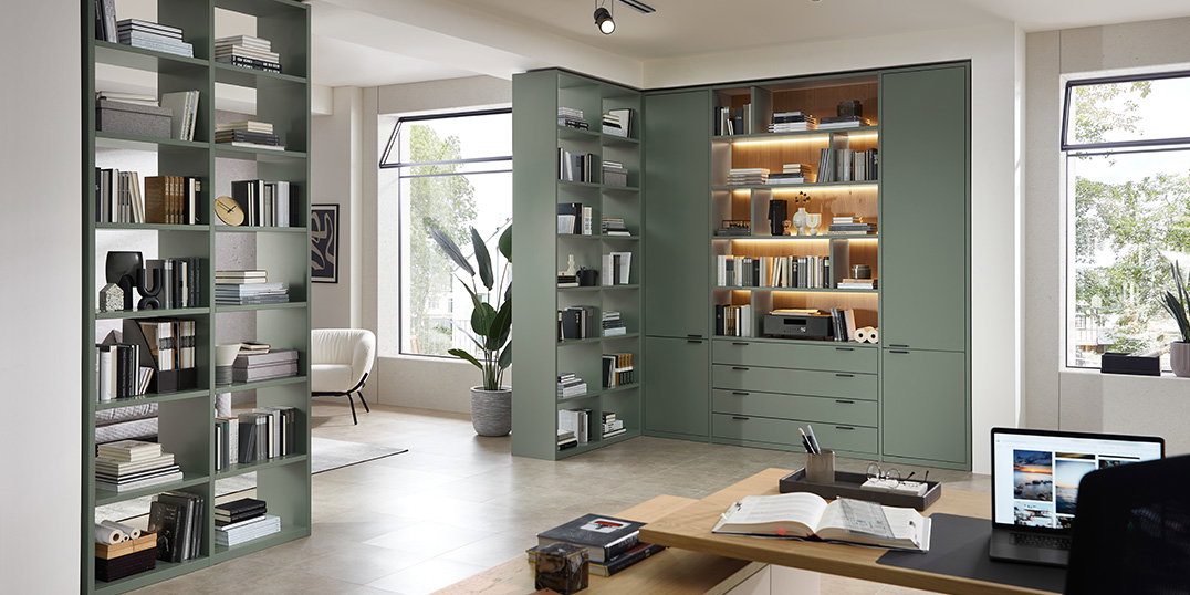Modernes Heimbüro mit grünen Bücherregalen.