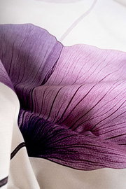 Nahaufnahme aus schräger Draufsicht auf ein weißes Textil mit großem Blütenmotiv in Violett- und Rosatönen, detailreiche Blütenblätter mit feiner Linienstruktur