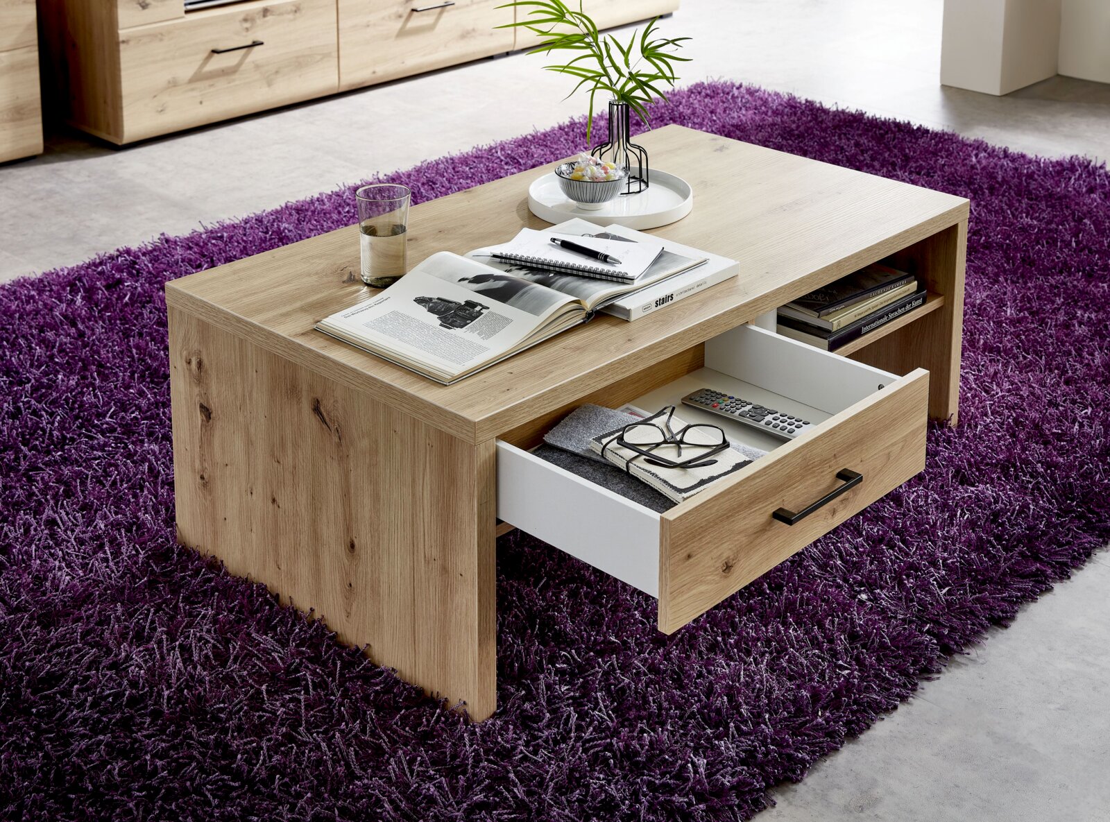 Moderner Couchtisch aus Holz mit Schublade, auf lila Teppich, aus seitlicher Perspektive fotografiert.
