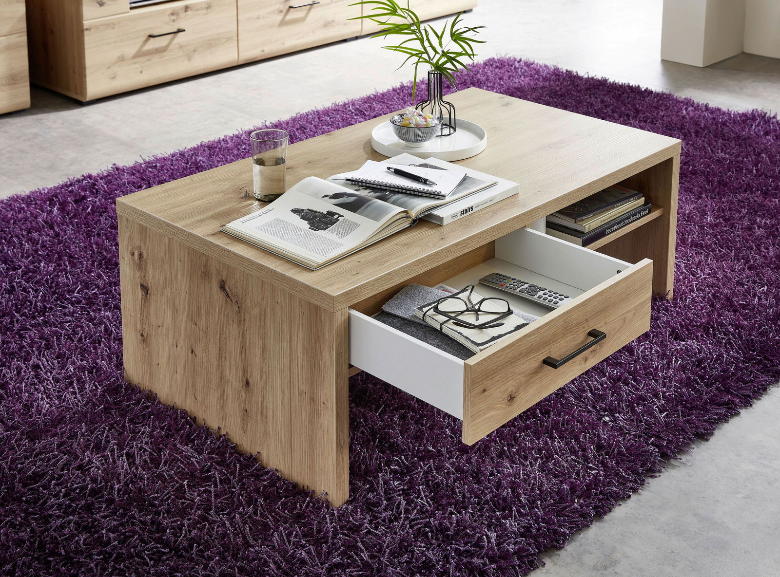Moderner Couchtisch aus Holz mit Schublade, auf lila Teppich, aus seitlicher Perspektive fotografiert.