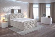 Boxspringbett in einem modernen Schlafzimmer mit seitlicher Perspektive, umgeben von stilvollen Möbeln und dekorativen Elementen.