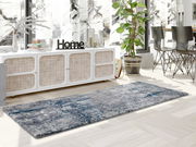 Moderner Designer Teppich in Grau- und Blautönen, in einem stilvoll eingerichteten Wohnzimmer mit Blick auf eine Kommode und Pflanzen.