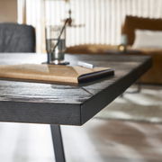 Nahaufnahme eines modernen Esstisches aus dunklem Holz mit Metallbeinen, im Hintergrund unscharf ein Wohnzimmer. Perspektive von der Tischkante.