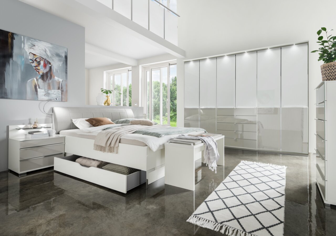 Modernes Futonbett in einem hellen Schlafzimmer mit großen Fenstern, stilvollen Möbeln und einem Kunstwerk an der Wand, aus der Perspektive von vorne links.