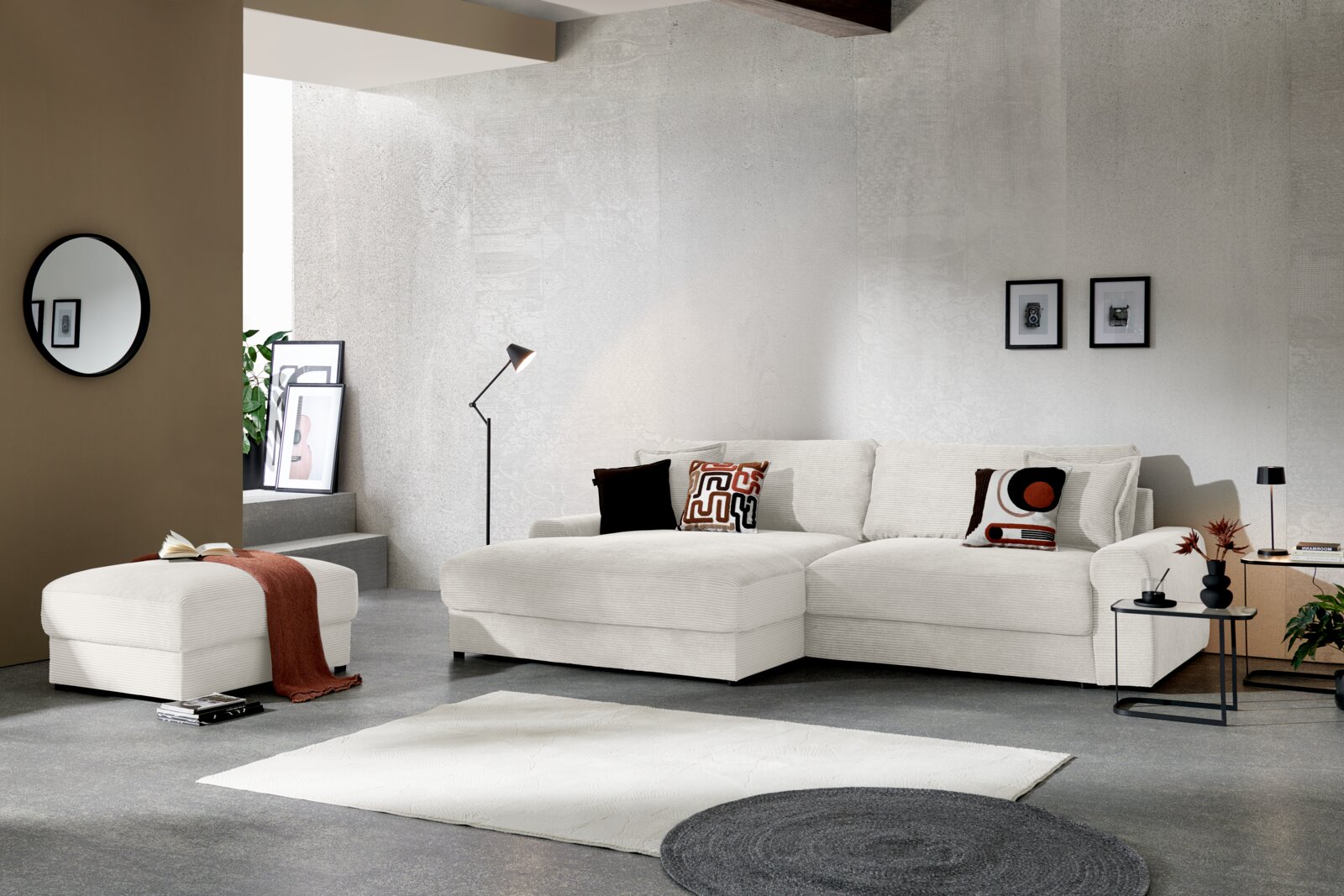 Z2 Ecksofa NAPOLI Modernes, helles Ecksofa mit Chaise longue in cremefarbenem Cordstoff im Wohnzimmer-Setting, Frontansicht leicht von links mit passendem Hocker, Kissen und Beistelltisch