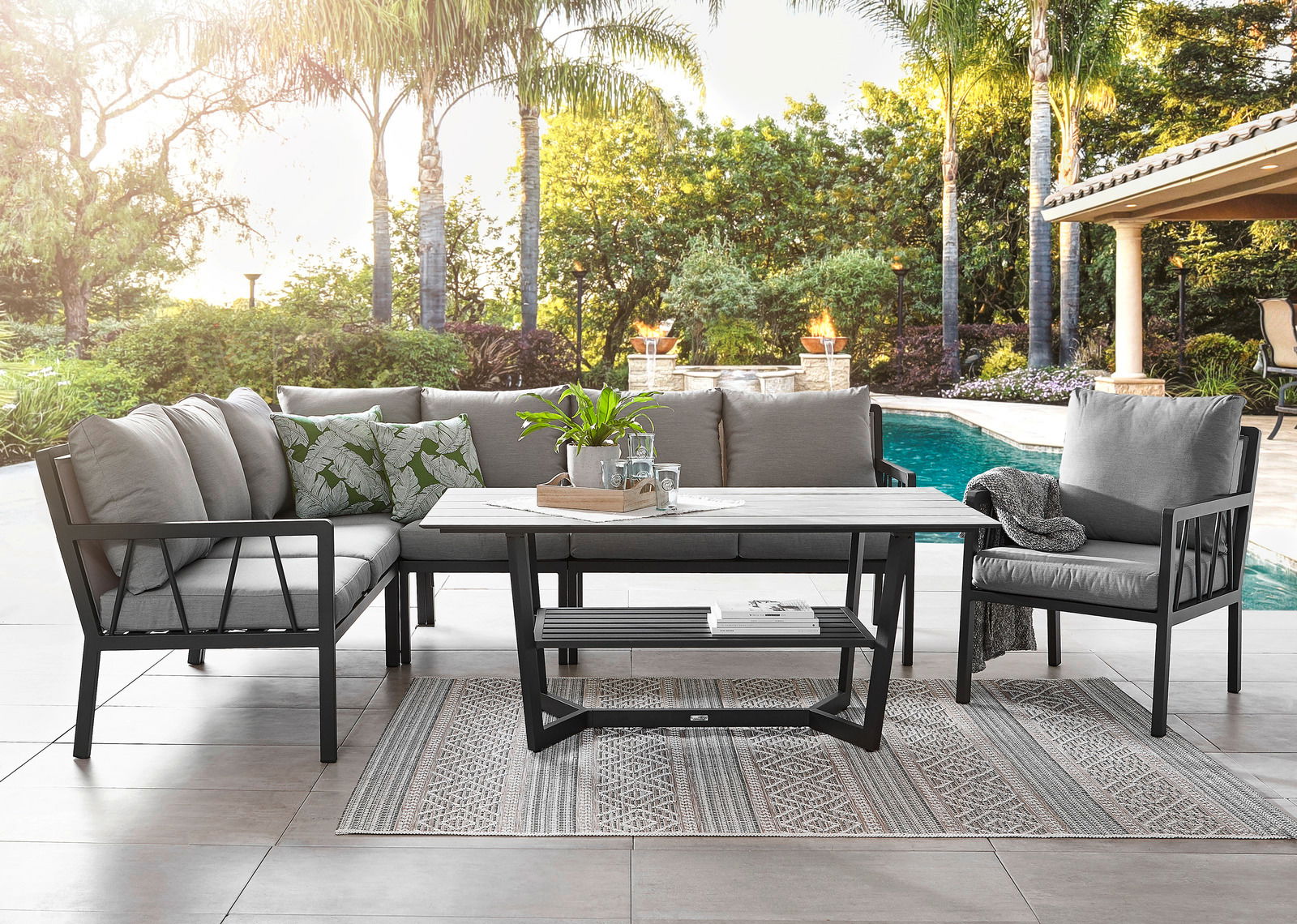 Gartenset bestehend aus einem Lounge-Sofa, einem Gartensessel und einem Tisch, auf einer Terrasse mit Blick auf einen Pool und umgeben von Palmen.