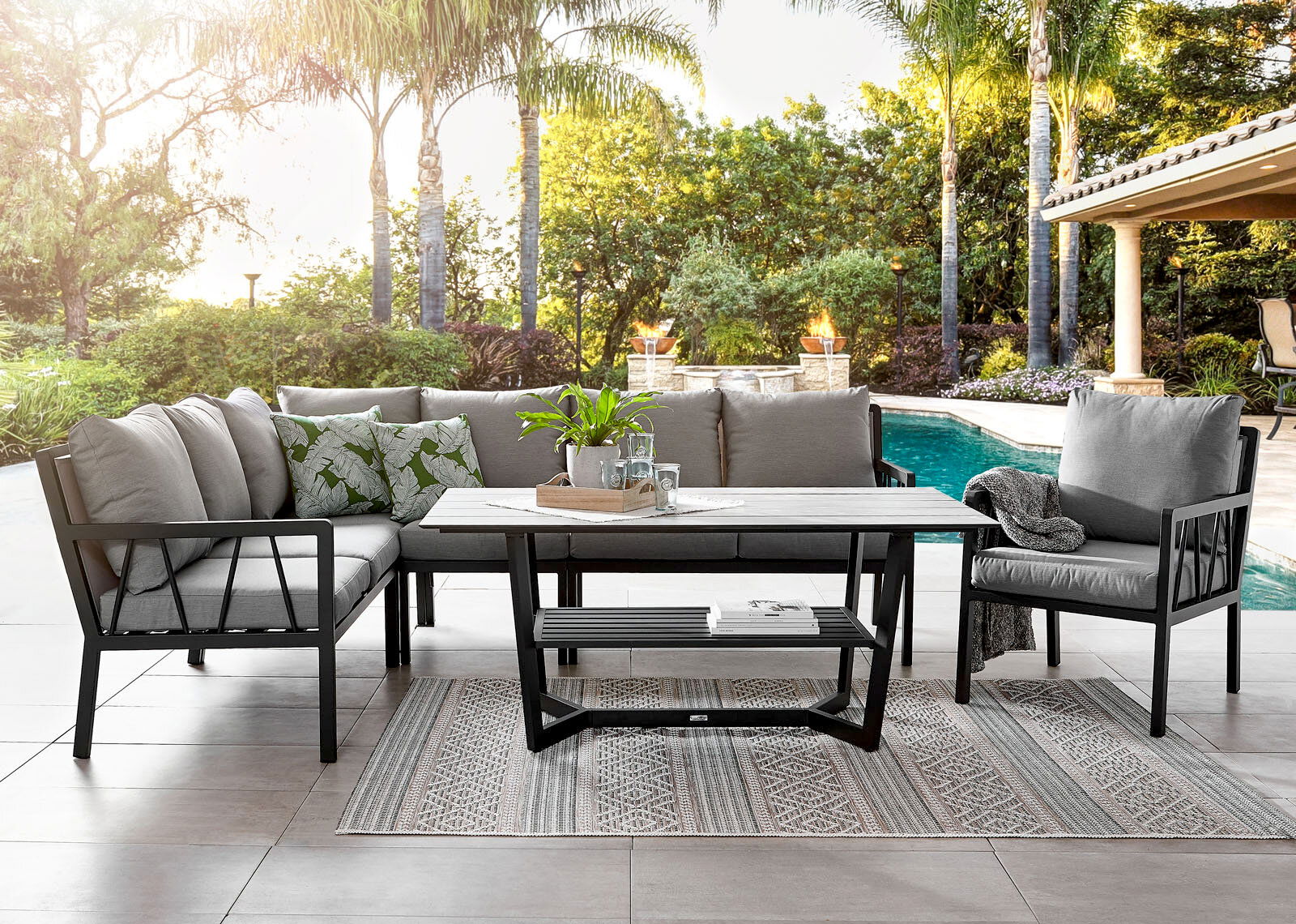 Gartenset bestehend aus einem Lounge-Sofa, einem Gartensessel und einem Tisch, auf einer Terrasse mit Blick auf einen Pool und umgeben von Palmen.