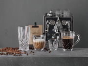 Vier elegante Gläser in verschiedenen Größen auf einer grauen Oberfläche, gefüllt mit Espresso und Kaffee, im Hintergrund eine Espressomaschine. Frontalansicht.