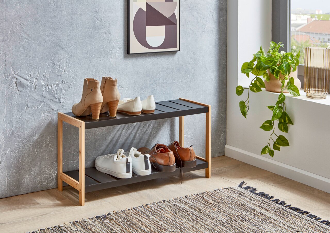 MID.YOU Schuhregal SMALL Zweistöckiges Schuhregal aus hellem Holz und schwarzen Ablagen im Flur, mit mehreren Paar Schuhen darauf, seitliche Frontansicht in leichtem Winkel.
