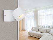 Moderner LED Strahler in Weiß, seitliche Perspektive, montiert an einer Wand in einem hellen Wohnzimmer mit großen Fenstern und einem beigen Sofa.