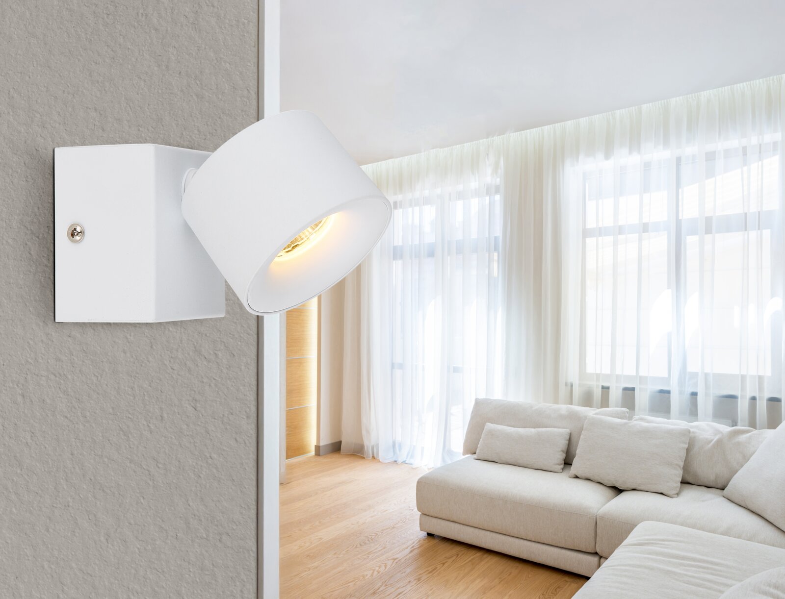 Moderner LED Strahler in Weiß, seitliche Perspektive, montiert an einer Wand in einem hellen Wohnzimmer mit großen Fenstern und einem beigen Sofa.