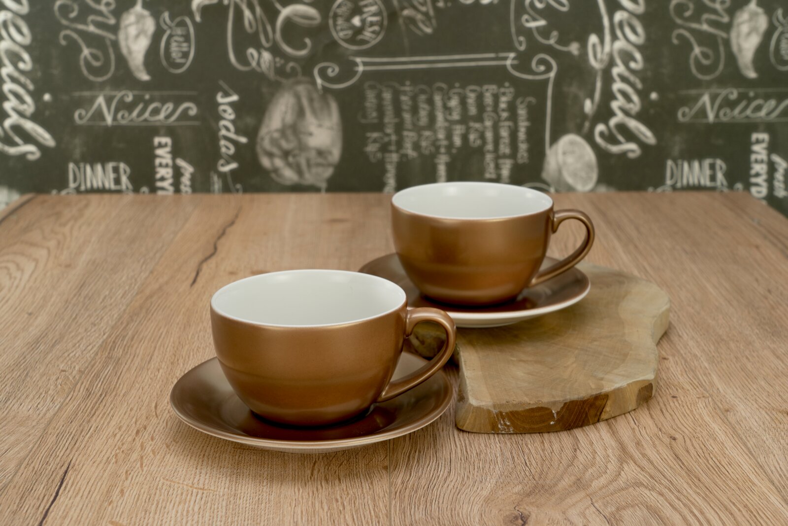 Creatable Cappuccinoset 4-tlg GOLDEN DAYS Zwei braune Keramik-Kaffeetassen mit Untertassen auf Holztisch, eine Tasse im Vordergrund und eine im Hintergrund auf einem Holzbrett, fotografiert in leicht erhöhter Frontansicht.