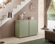 Moderne grüne Kommode mit zwei Türen, seitliche Perspektive, unter einer Treppe platziert, dekoriert mit Büchern und Kerzenhalter.