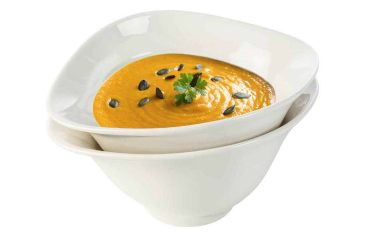 Zwei weiße Suppenschalen im Set, übereinander gestapelt, gefüllt mit Kürbissuppe, dekoriert mit Kürbiskernen und Petersilie, seitliche Perspektive.