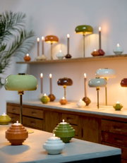 Tischleuchte SURIN in verschiedenen Farben auf einem Tisch, mit einer grünen Lampe im Vordergrund und mehreren Lampen im Hintergrund, seitliche Perspektive.