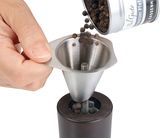 Einfülltrichter aus Edelstahl, der Pfefferkörner in eine Pfeffermühle füllt, aus der Perspektive von oben.