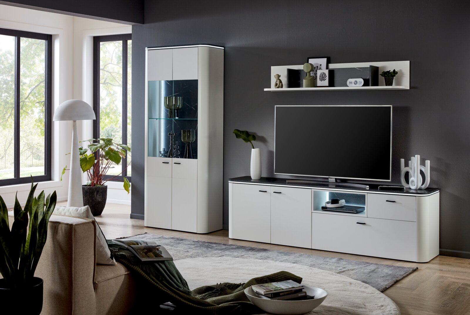 Moderne Wohnzimmer-Wandkombination in Weiß mit Vitrine, TV-Schrank und Regal, seitliche Perspektive.