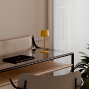 Gelbe, minimalistische Tischlampe auf einem Glas-Beistelltisch neben einem Ledersofa in hellem Wohnraum, seitliche Perspektive