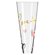 Nahaufnahme eines Champagnerglases mit goldener Schrift 'Love' und bunten Herzen.