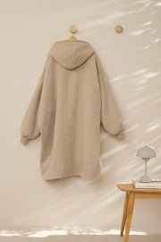 Beiger Lounge Hoodie von hinten an der Wand hängend, mit Kapuze und langen Ärmeln, in einem minimalistisch eingerichteten Raum.