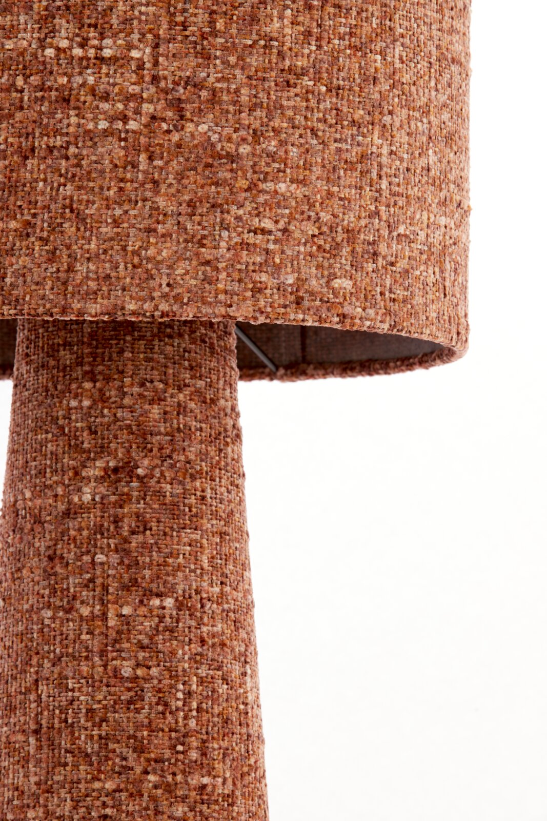 Close-up vanuit zijaanzicht van een tafellamp met een cilindervormige kap en voet, bekleed met warm roestbruin gemêleerd structuurtextiel.