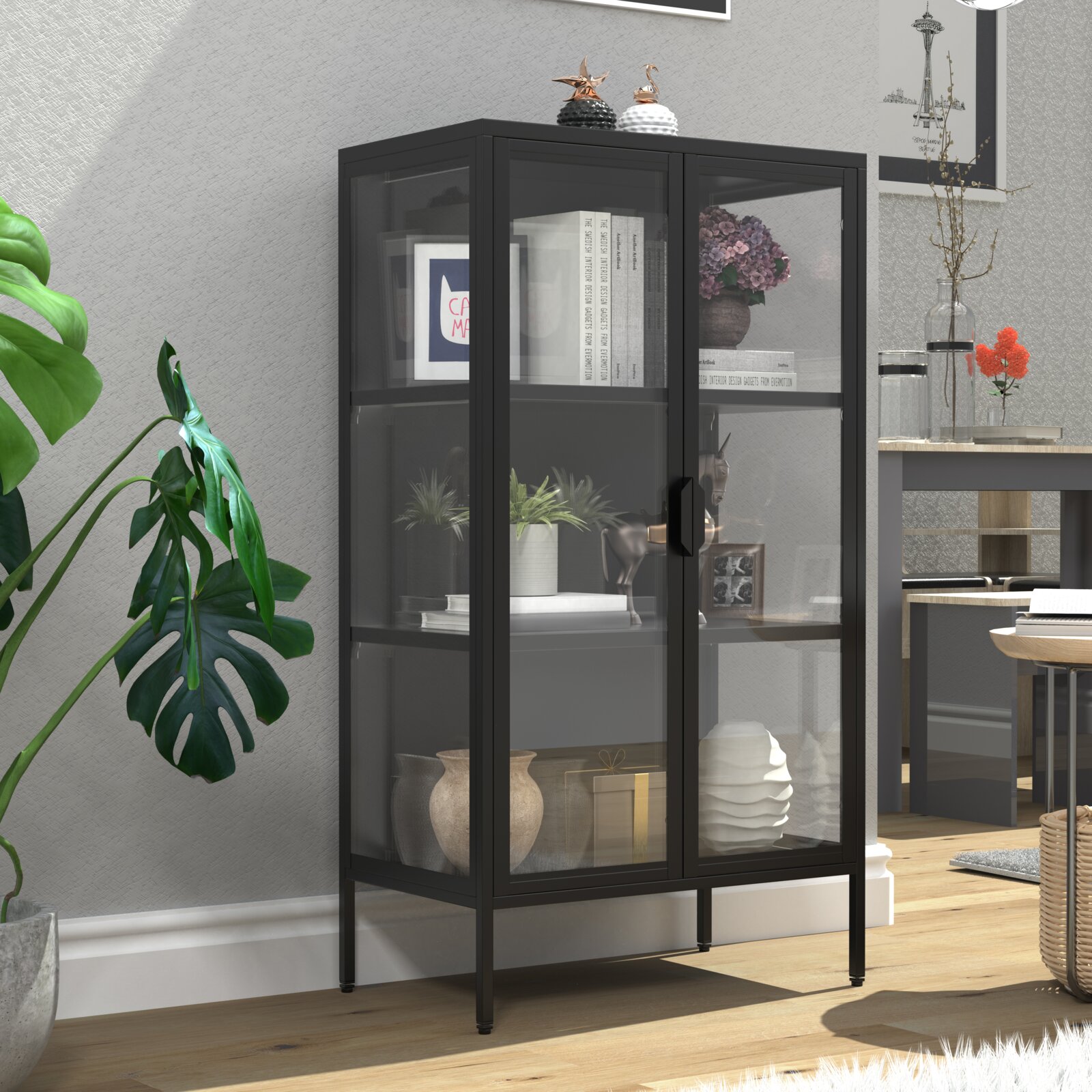 Schwarzer Metall-Vitrinenschrank mit zwei Glas-Flügeltüren und Ablagefächern, gefüllt mit Deko und Büchern, in Wohnraum-Setting; Perspektive: frontale Ansicht leicht von links