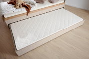 Bettkasten in heller Holzoptik, von oben fotografiert, mit herausziehbarem Unterschiebebett und weißer, gesteppten Matratze.