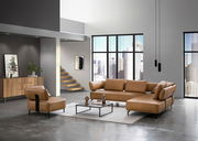 Moderne Wohnzimmermöbel in einem hellen Loft mit großen Fenstern, bestehend aus einer braunen Polsterecke und einem passenden Sessel, aus der Perspektive von vorne links betrachtet.