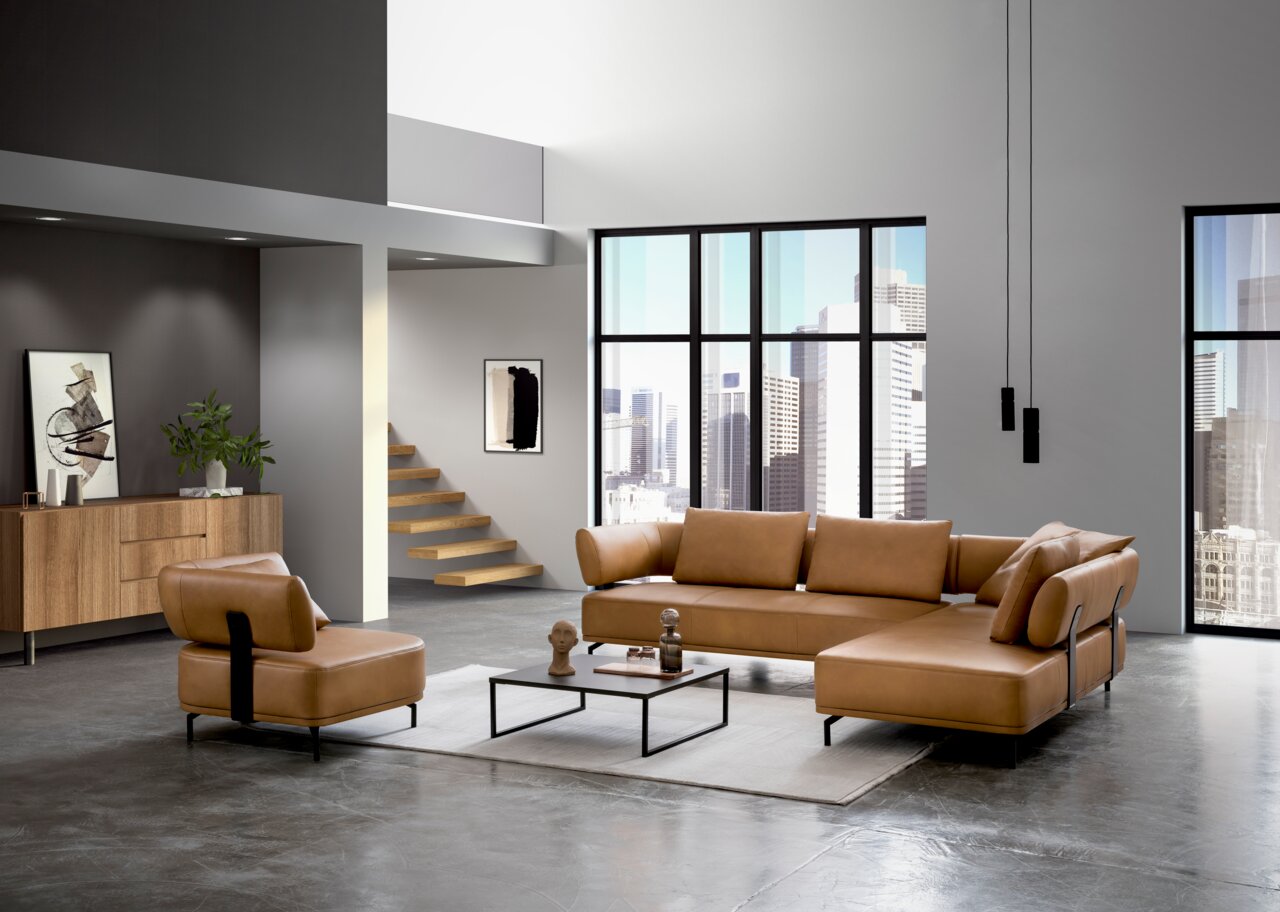 Dieter Knoll Sessel PALIO Moderne Wohnzimmermöbel in einem hellen Loft mit großen Fenstern, bestehend aus einer braunen Polsterecke und einem passenden Sessel, aus der Perspektive von vorne links betrachtet.