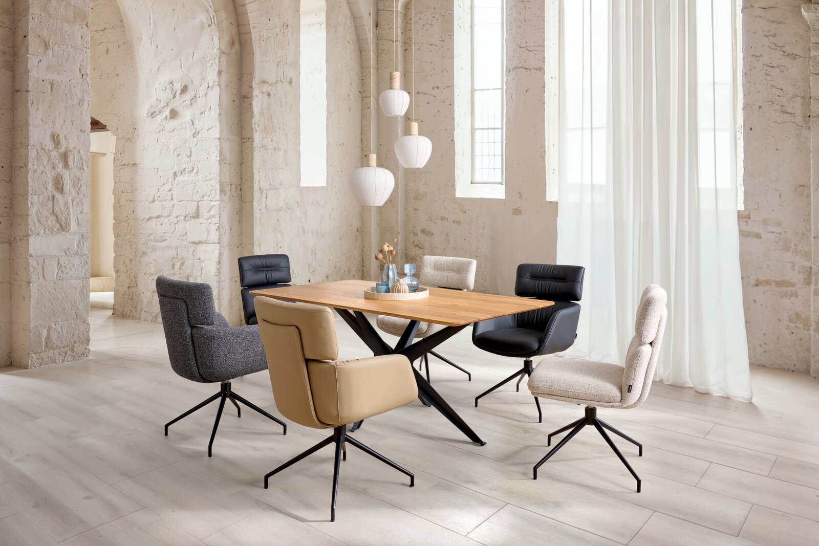 Dieter Knoll Eettafel TAVOLO Moderne eethoek met rechthoekige houten eettafel op zwart metalen X-onderstel, omringd door zes draaibare kuipstoelen in verschillende bekledingen, gefotografeerd in een lichte loft vanuit een schuin vooraanzicht op ooghoogte