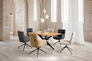 Modernes Esszimmer-Set mit rechteckigem Holzesstisch auf schwarzem X-Gestell und fünf gepolsterten Drehstühlen in verschiedenen Farben in hellem Loft, perspektivisch in schräger Seitenansicht von vorn rechts